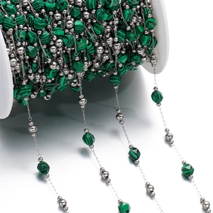 Close-up of DIY jewelry chain with green faceted stones and silver beads on white spool
