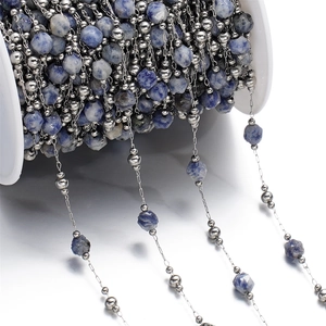 Macro shot of blue faceted natural stone beads and silver metal chain on a white spool