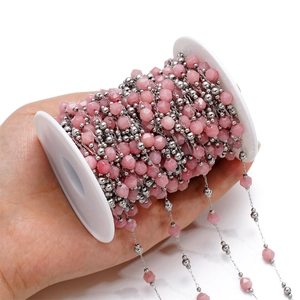 Macro detail of pink faceted stone beads and silver chain on a spool for DIY jewelry