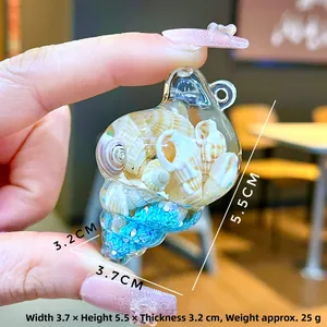 Detail of acrylic sea snail pendant with blue moving sand and shells held in hand