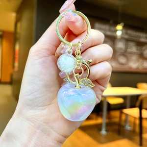 Macro detail of iridescent apple-shaped resin keychain with sparkling gold leaf charm