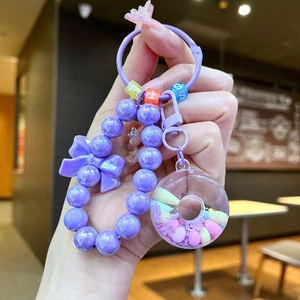 Macro detail of purple beaded keychain with donut pendant and bow accent on bags