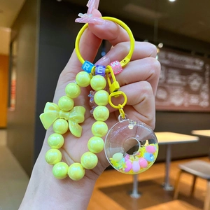 Macro shot of yellow beaded keychain with bow, donut charm and letter beads held in hand