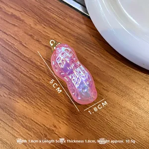 Détail macro du pendentif cacahuète rose irisé avec dimensions sur fond en bois naturel