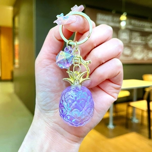 Close-up of a pearlescent purple glitter pineapple keychain with golden metal clasp