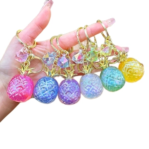 Set of six colorful pearlescent resin pineapple pendants with gold keychains held in hand