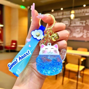 Close-up of lucky cat liquid keychain with blue glitter sand and golden bell detail