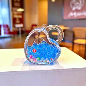 Macro shot of heart-shaped acrylic charm filled with blue luminous beads and small flowers