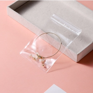 Close-up of golden thin bangle with pink beads and tassel in transparent PVC jewelry bag