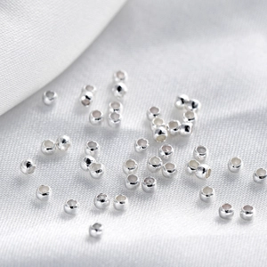 Micro shot of polished silver-tone 18K gold-plated spacer beads on white silk fabric