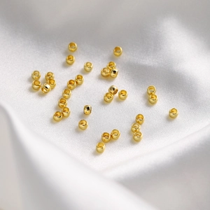Macro shot of 18K gold-plated hollow metal beads on a white velvet background