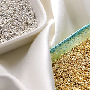 Macro shot of 18K gold and silver plated crimp beads for DIY jewelry on silk