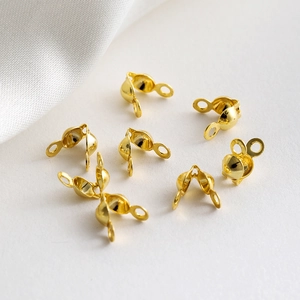 Macro detail of 18K gold plated bead tip jewelry connectors on grey textured paper
