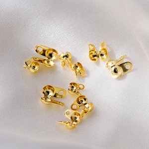 Detailed view of 18K gold-plated bead chain clamshell crimps on white silk background