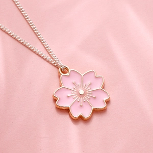 Kersenvloesem ketting met roze emaille en gouden rand op een zachte roze achtergrond