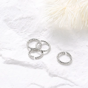 Détail de quatre anneaux de saut torsadés en argent pour bijoux DIY sur fond de pierre blanche