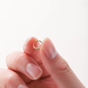 Détail d'un petit anneau torsadé plaqué or 18 carats tenu entre les doigts de la main