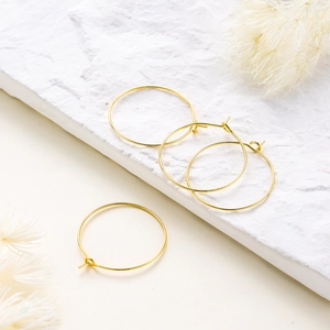 Vista macro de pendientes de aro chapados en oro 18K sobre mármol con flores decorativas