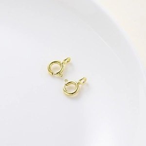 Macro shot of 18K gold-plated spring ring clasp jewelry connectors on white ceramic