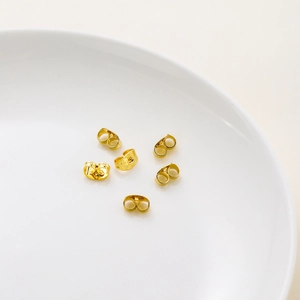 Close-up of 14K gold plated butterfly earring backs on a minimalist white ceramic tray