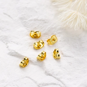 Close-up of six gold-plated butterfly earring backs on a white marble stone surface