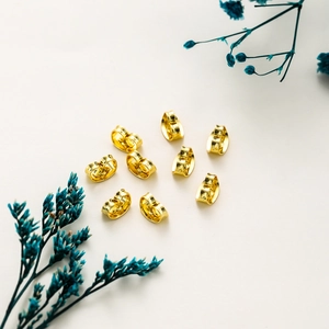 Nine 14k gold plated butterfly earring backs scattered on a white textured background