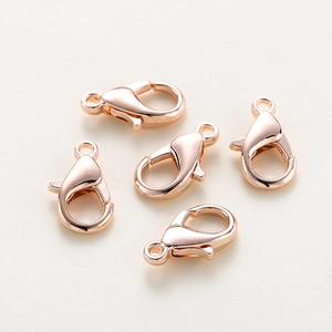 Five rose gold lobster clasps for DIY jewelry making laid on a textured beige surface
