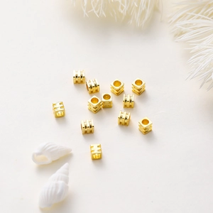 Primer plano de cuentas espaciadoras cuadradas doradas para joyas DIY en una concha blanca