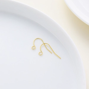 Close-up of polished gold French ear hooks on white ceramic tray for DIY jewelry making