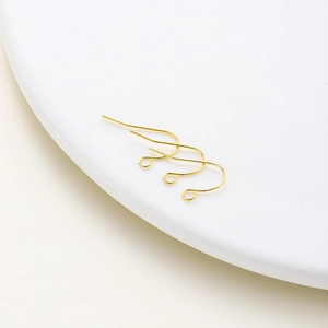 Close-up of three gold-plated fishhook earring wires on a white ceramic plate for DIY jewelry