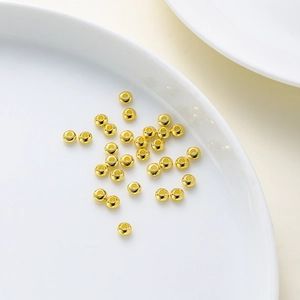 Macro shot of 18K gold plated polished round beads on a white ceramic tray for DIY jewelry