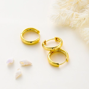 Macro detail of high-polished 14K gold plated hoop earrings on minimalist background