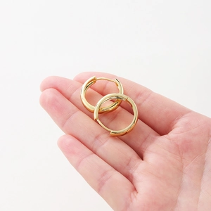 Detail showing hand holding 14K gold plated hoop earrings with a polished surface