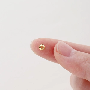 Polished 18K gold-plated spacer bead shown on fingertip for size scale DIY jewelry