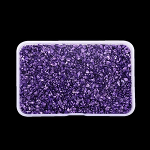 Detail view of irregular dark purple metallic crushed glass stones in a clear plastic box
