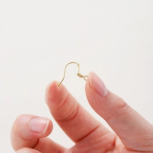 Gros plan d'un crochet de boucle d'oreille plaqué or 14 carats tenu entre les doigts