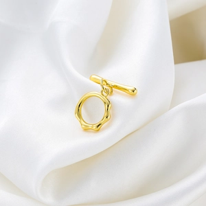 Detail eines 18K vergoldeten Knebelverschlusses mit unregelmäßigem O-Ring auf weißer Seide