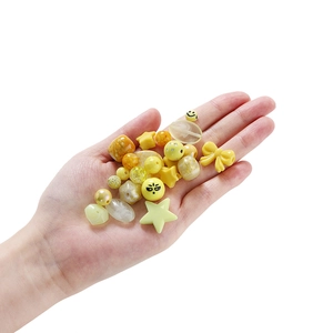 Nahaufnahme gelber Bastelperlen aus Acryl mit Sternen und Schleifen in der Hand