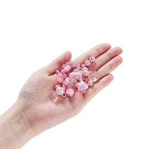 Rosa Acryl-DIY-Perlenmix mit Herzen, Schleifen und Perlen handpräsentiert auf weißem Grund