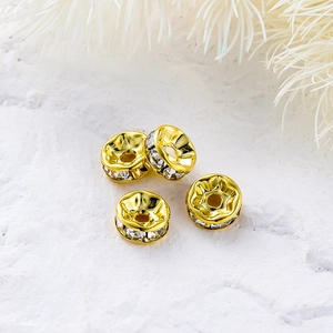 Detalle de cuentas espaciadoras chapadas en oro 14K con cristales sobre fondo de piedra blanca