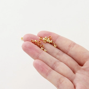 Close-up of tiny 18K gold-plated spacer beads on fingertips for DIY jewelry making