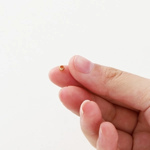 Close-up of a 2mm 18K gold-plated spacer bead held between fingers to show tiny size