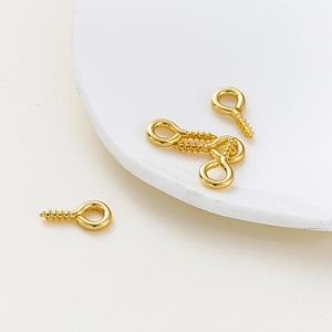 Macro shot of 14K gold plated eye pins for DIY jewelry making on white ceramic surface