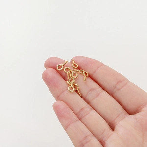 Macro shot of 14K gold plated screw eye pins held by fingers showing micro size scale