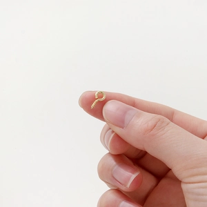 Macro shot of tiny gold-plated eye pins for DIY jewelry making held in hand for size