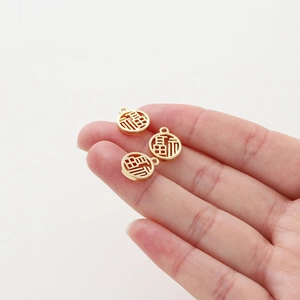 Detail of three 18K gold-plated round Fu pendants held in hand for size comparison