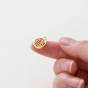 Close-up of a small 18K gold-plated Fu pendant held between fingers showing tiny scale