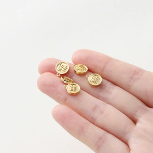 Detailed close-up of a mini 18K gold-plated round Fu charm held between fingers