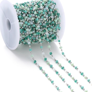Detail of crystal stone colorful bead chain with green tassels on white plastic spool