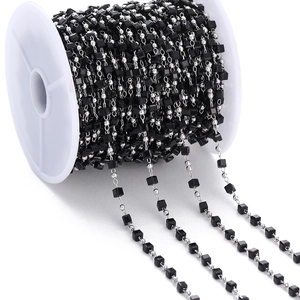 Macro detail of black faceted crystal and silver bead chain on a white spool for DIY jewelry